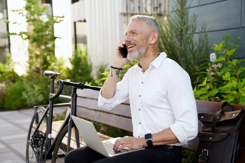 Establishing links. Modern middle aged businessman in white shirt talking on the phone, working on